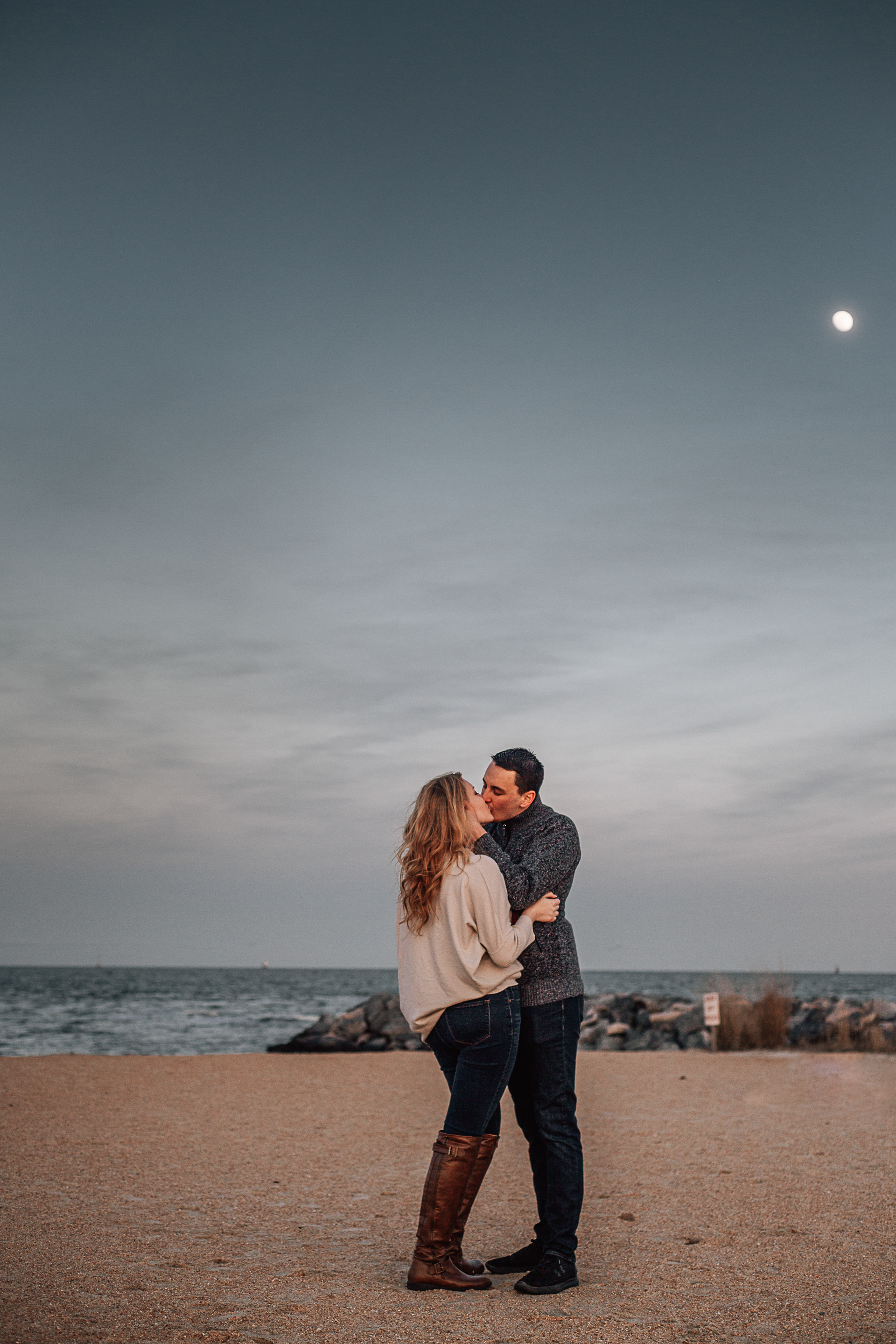 couple standing on the beach kissing during engagement photography session at fort monroe