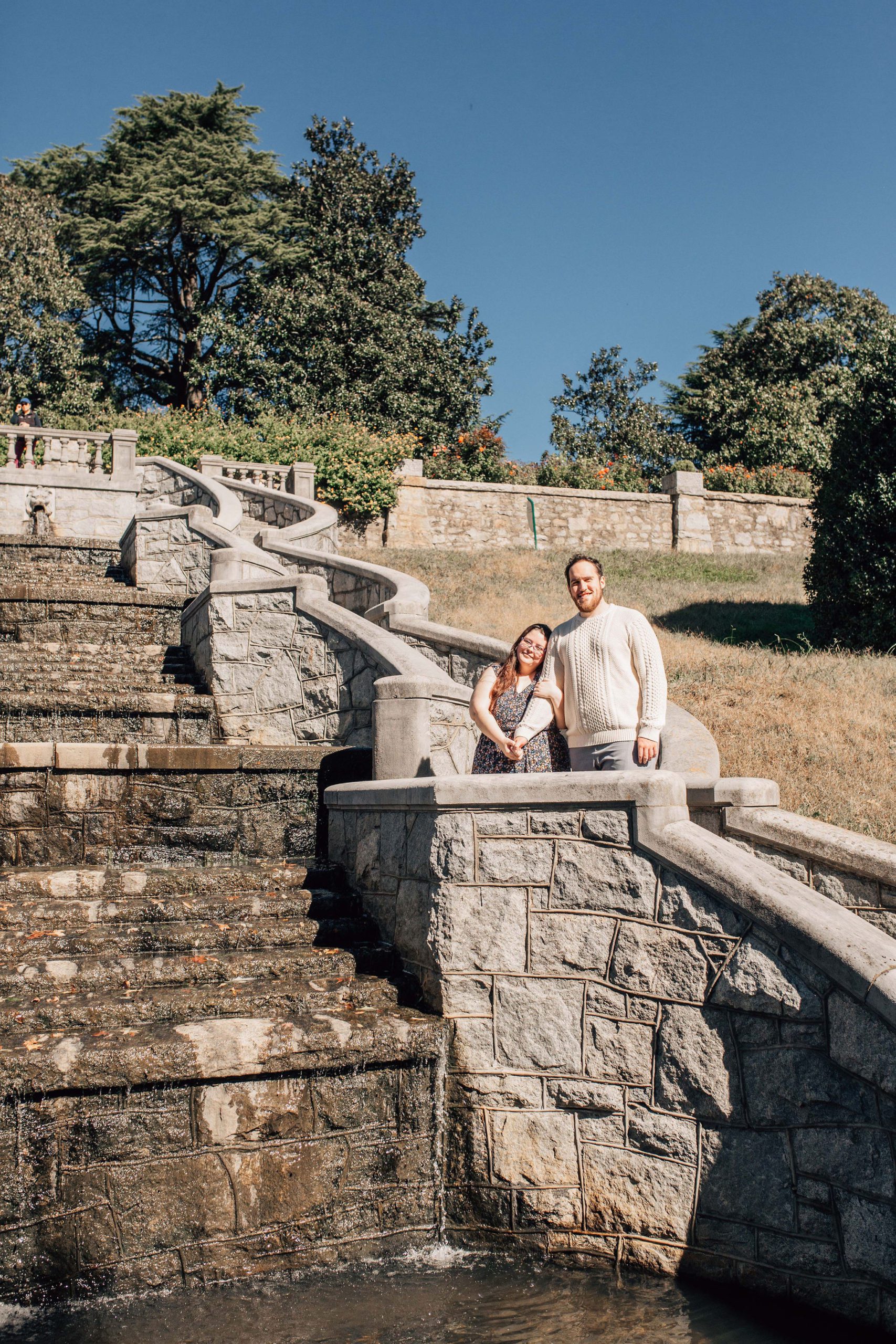 man and woman holding hands and standing close together on stone stairs in a Hampton Roads garden for their natural pose engagement session