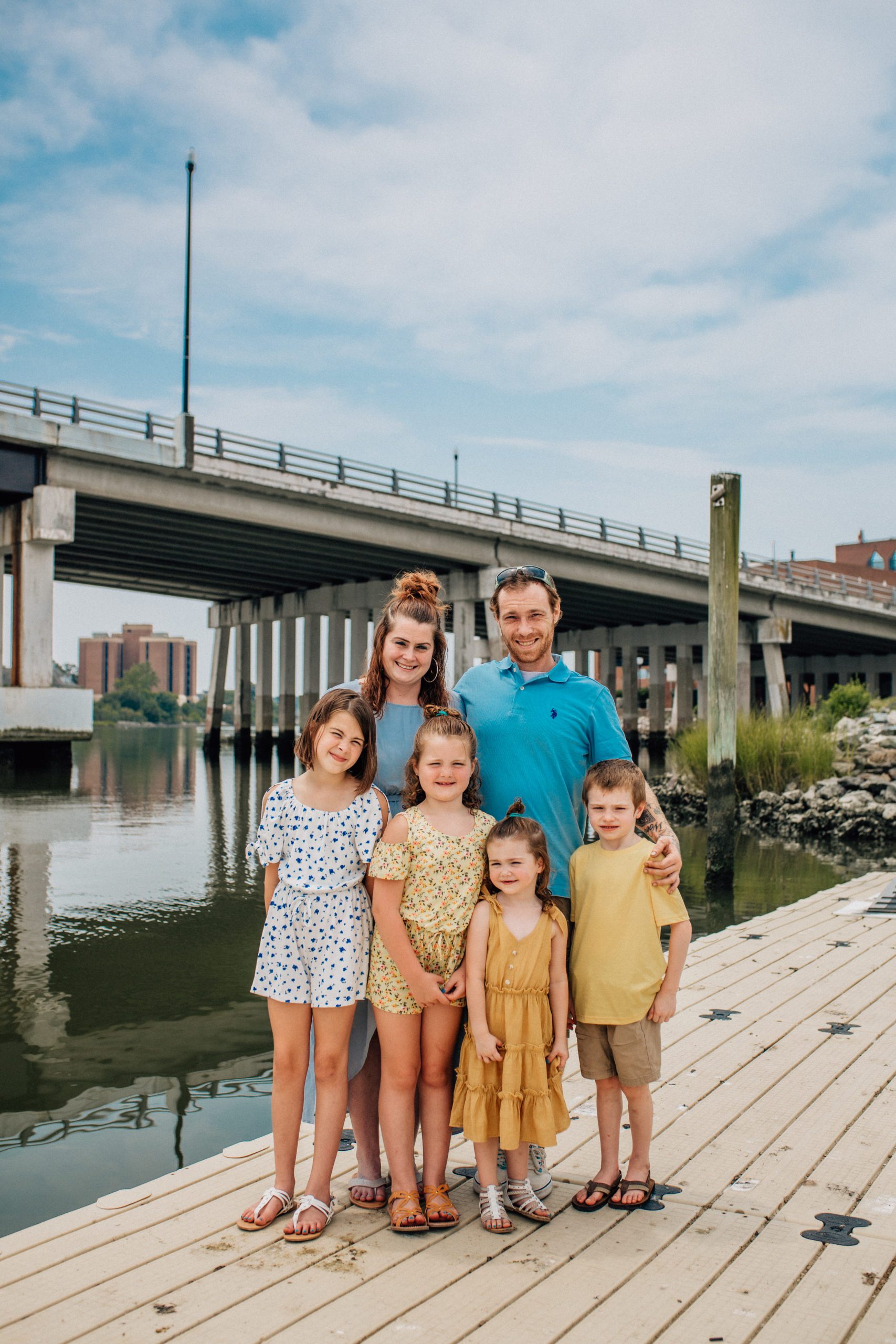 family portraits of a family of six standing together next to a bridge near the water captured by Hampton Roads family photographer