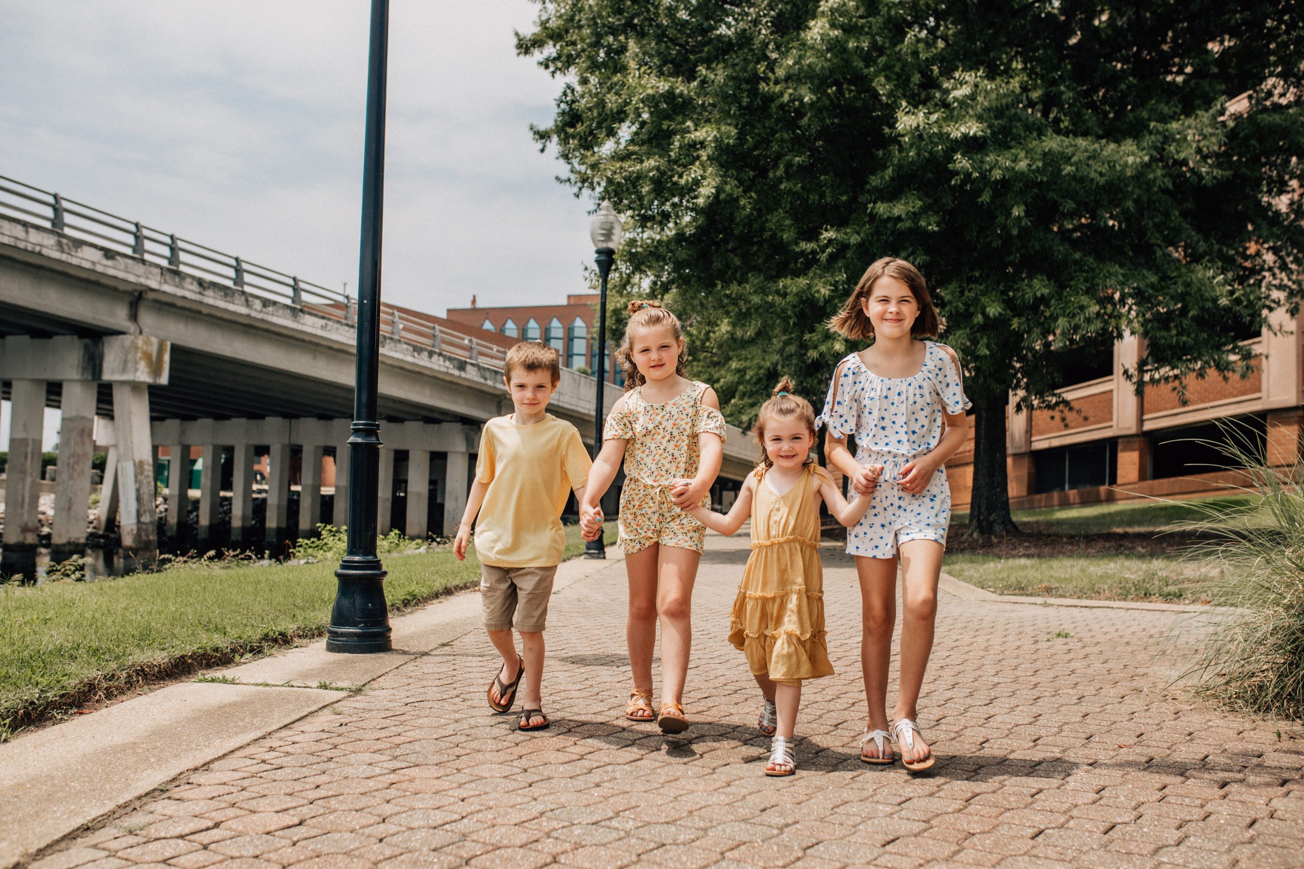 four little children holding hands and walking down a brick path