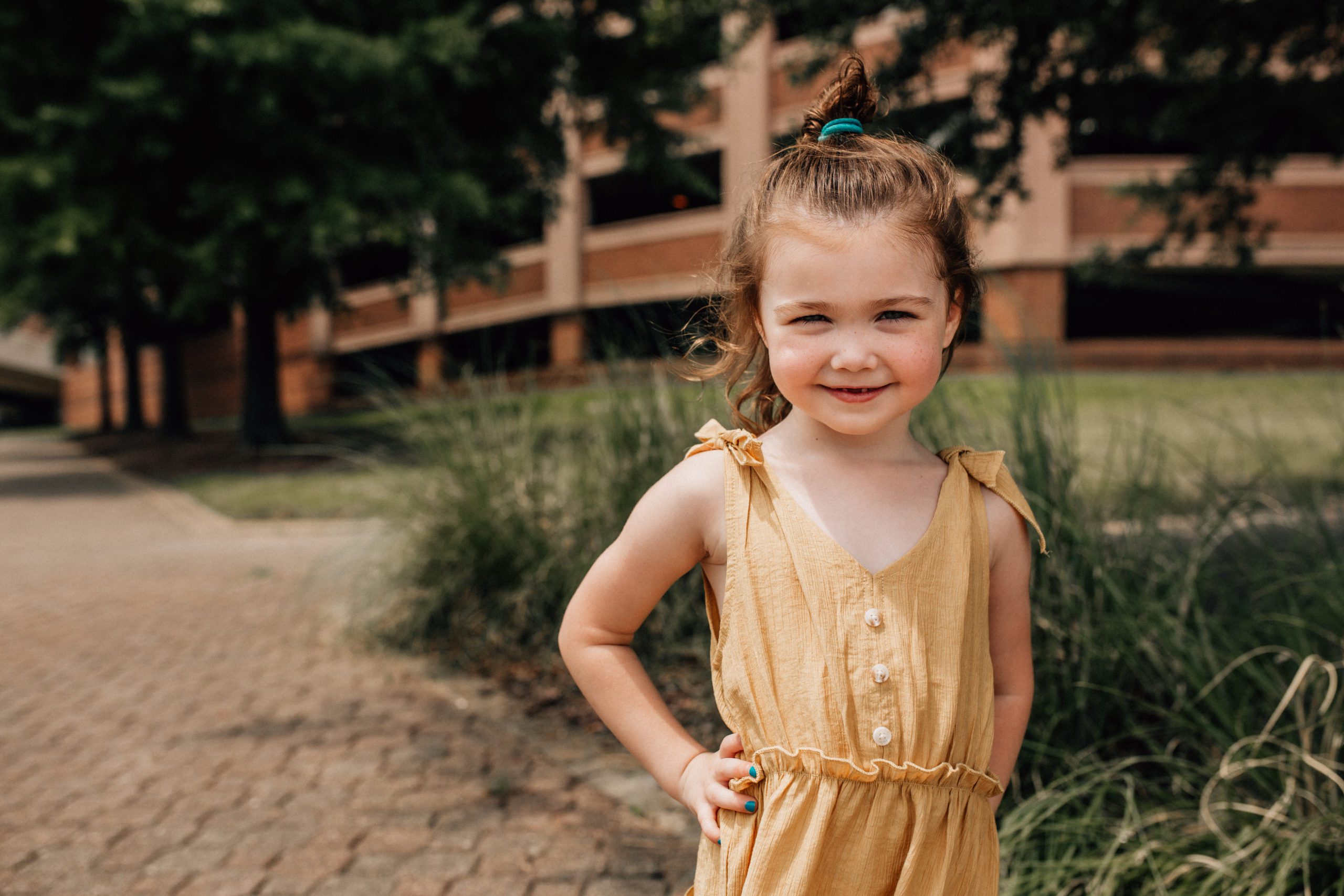 toddler girl in a yellow jumper with her hands on her hips smiling for her summer family photos in Hampton Roads
