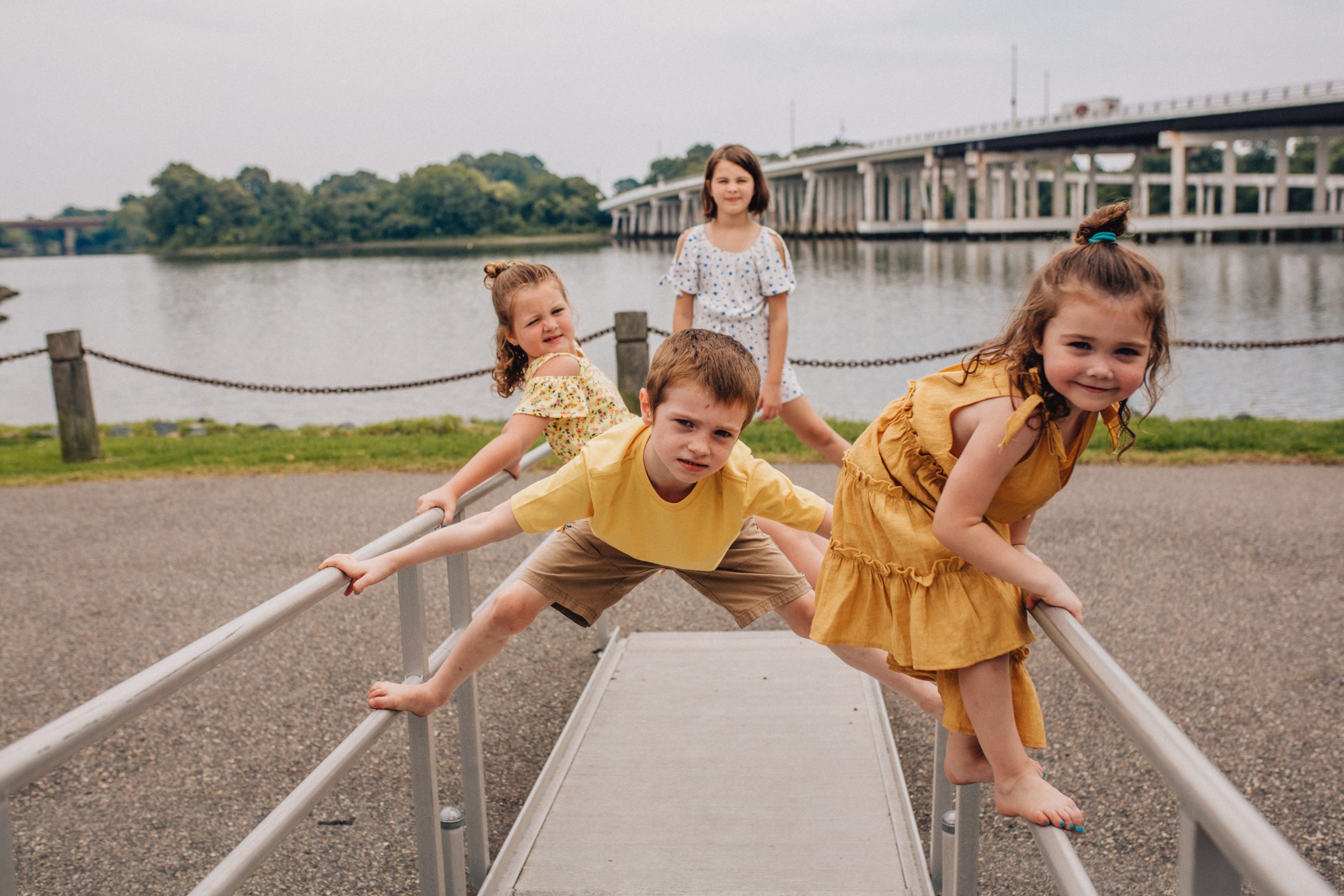 Hampton Roads family photographer capture candid moment of four young siblings playing on a railing next to a river