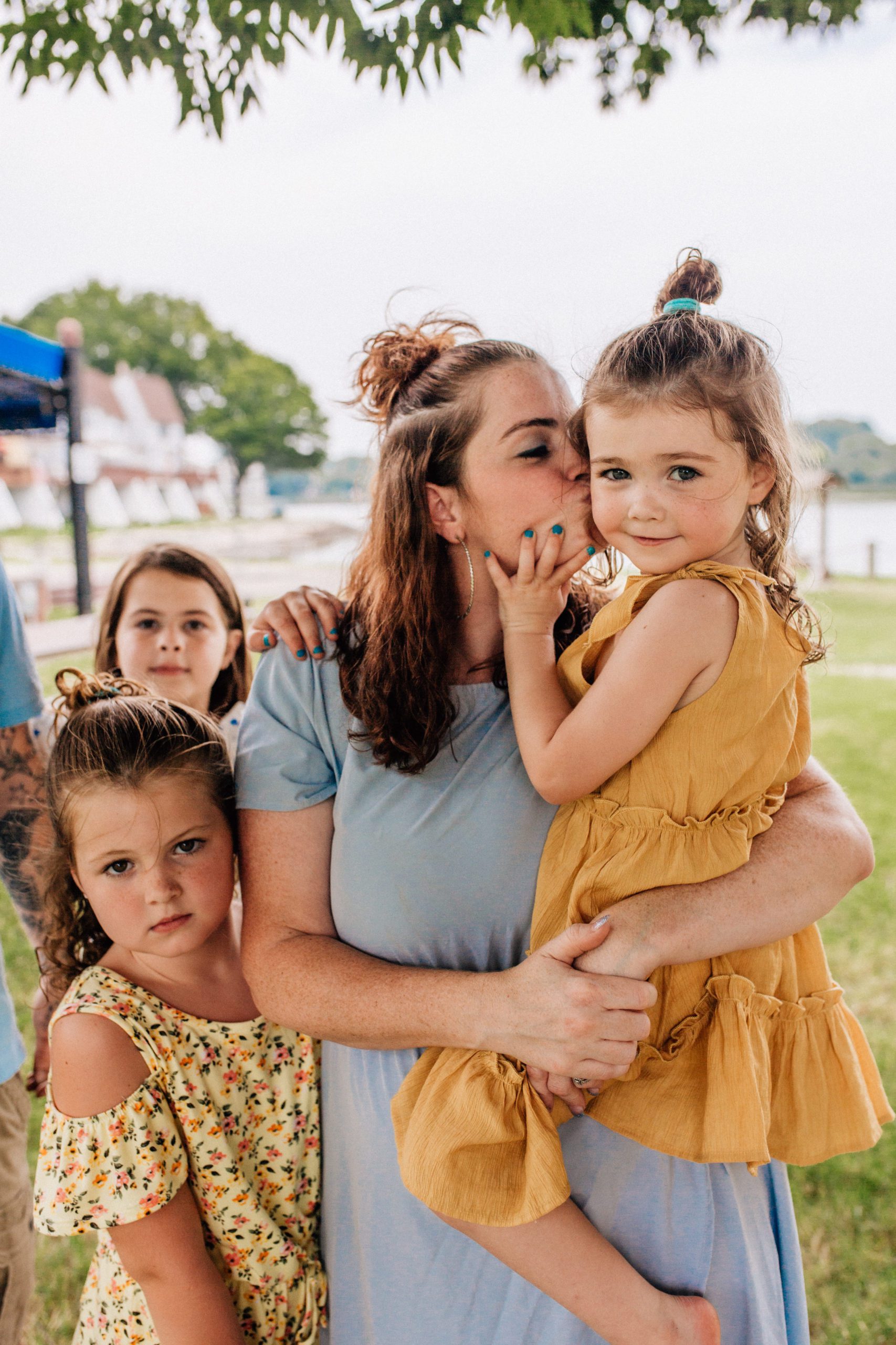 mother holding her daughter and kissing her on the cheek as her other children surround her