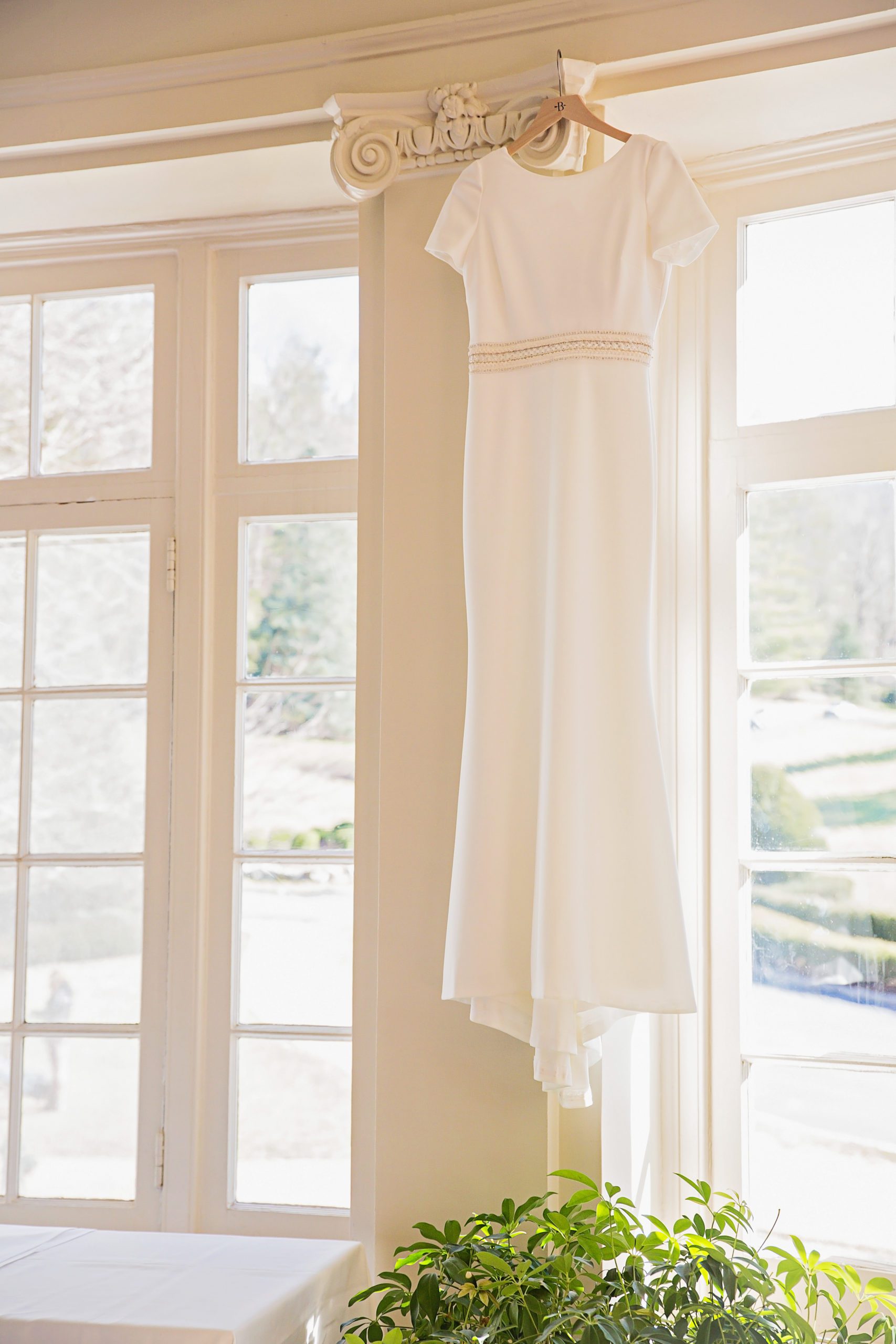 satin white wedding. dress with a sequence belt hanging in a window of a Virginia wedding venue